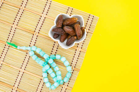 Ramadan Kareem Festival. Close up of dried dates fruit in bowl with rosary on yellow background. Copy spaceの写真素材