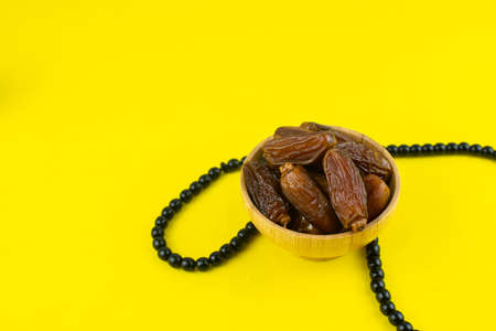 Ramadan Kareem Festival. Close up of dried dates fruit in bowl with rosary on yellow background. Copy spaceの写真素材