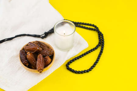 Ramadan Kareem Festival. Close up of dried dates fruit in bowl with candle and rosary on yellow...