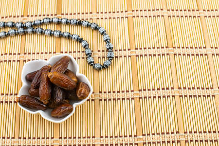 Ramadan Kareem Festival. Close up of dried dates fruit in bowl with black rosary on wooden...