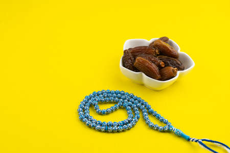 Ramadan Kareem Festival. Close up of dried dates fruit in bowl with rosary on yellow background....