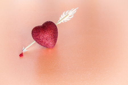 Heart pierced by an arrow on pink background. Blood dripping from the tip of the arrow. Place for textの写真素材