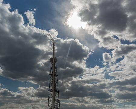 Smoking chimney of oil refinery against cloudy sky and sunの写真素材