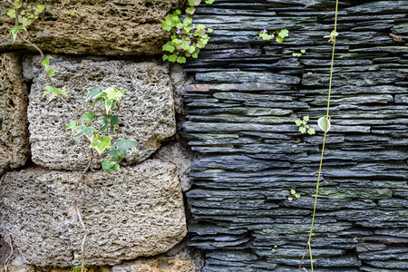 Junction of walls with two different textures. Layers of uneven black stone side by side to grungy pumice bricks. Natural background and texture for designの写真素材
