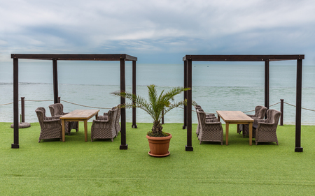 Wooden tables and wicker chairs overlooking sea and heaven. Palm tree in flowerpotの写真素材