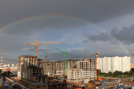 Full rainbow over the construction site with building cranesの写真素材