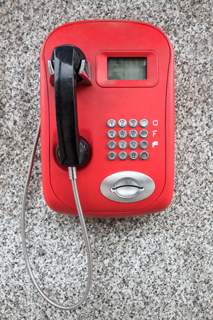 Red public telephone with black handset on the granite wall