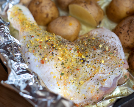 Close-up of raw chicken leg with spices. Defocused unpeeled potatoes in the background. Selective focus, partial blurredの写真素材