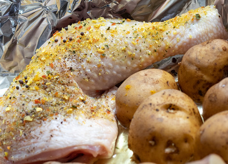 Close-up of raw chicken leg with spices. Defocused unpeeled potatoes in the foreground. Selective focus, partial blurredの写真素材