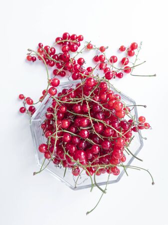 Freshly picked red currant in glass bowl on white background. Redcurrant branches close to glass jar. Top viewの写真素材