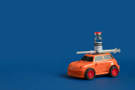 Orange toy car with vaccine vial and medical syringe on blue background. Concept of immunization, disease prevention or delivery of vital medicinesの写真素材