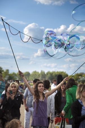Berlin, Germany - June 10th, 2012: A young adult woman making giant soap bubbles on an early summer Sunday afternoon at Mauerpark, with the park's crowd all around and flea market in the background.のeditorial素材
