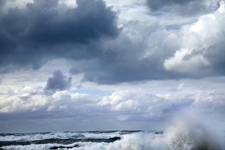 A giant wave raising above the sea's water surfaced, its surf scattered by the strong wind under the...