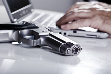A 9mm handgun resting on a table, and defocused in the background the hands of a mature adulat man...