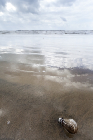 A used burnt-out incandescent light bulb abandoned on a sandy beach in inclement weather. Relates to energy conservation and environmental issues in general.の写真素材
