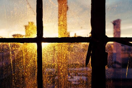 Afternoon yellow sun is back-lighting a window stained with drop marks, accentuating the texture and shapes の写真素材