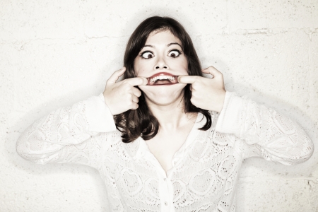 Portrait of a beautiful young woman making a monster face. Her big eyes wide open and cross eyed, looking in sheer terror; her hands opening her mouth as wide as possible. Total look is very goofy. Not so frightening after all.の写真素材