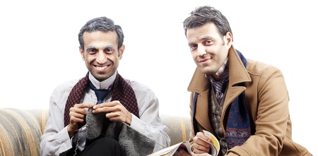 Two adult man (mid 30's and mid 20's) wearing old-man clothes and makeup, sitting on a used up vintage sofa. One of them is knitting while the other one flipping the page of the newspaper he's holding. Isolated on white background.の写真素材