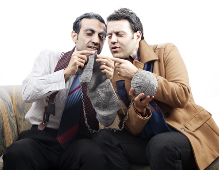 Two adult man (mid 30's and mid 20's) wearing old-man clothes and makeup, sitting on a used up vintage sofa. One of them is knitting while the other one is holding the ball of yarn. They seem to be discussing the knitting. Isolated on white background.の写真素材