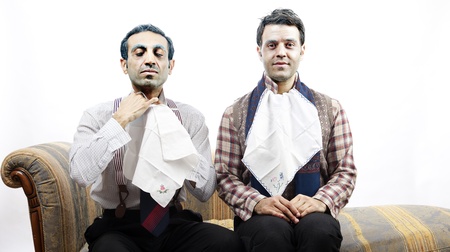 Two adult man (mid 30's and mid 20's) wearing old-man clothes and makeup, sitting on a used up vintage sofa. The left one is adjusting a cloth napkin on his neck while the one on the right sits looking at the camera, waiting patiently for his coming meal.の写真素材