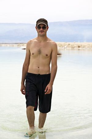 A young adult tourist walking in the shallow waters of the Dead Sea, Israel.の写真素材