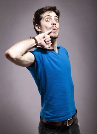 Studio shot of a young adult Caucasian man in his late 20's giving the camera a wide eyed comic expression his his pinky on the edge of his mouth.の写真素材