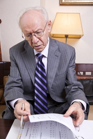 An elderly (in his 80's) business man wearing suit and tie sitting in a hotel's business lounge, going over some papers.の写真素材
