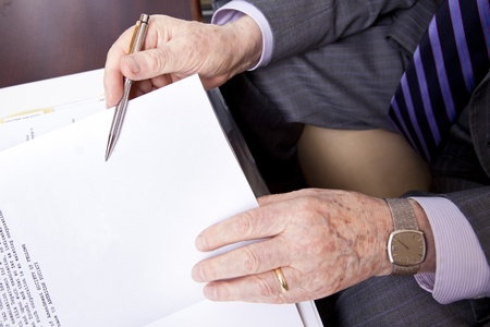 Close up on hands of a senior (in his 80's) businessman about to sign a contract. He's holding a fancy pen in his right hand and wearing a gold wedding ring and watch on his left. Seen from a high angleの写真素材