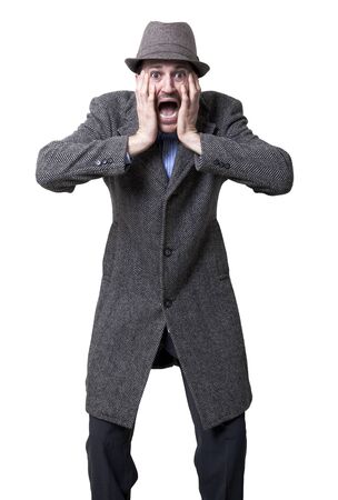 A young adult dressed in a gray overcoat and a gray hat, with a surprised and fearful expression on his face, holding it with both hands.
Isolated on white background.の写真素材