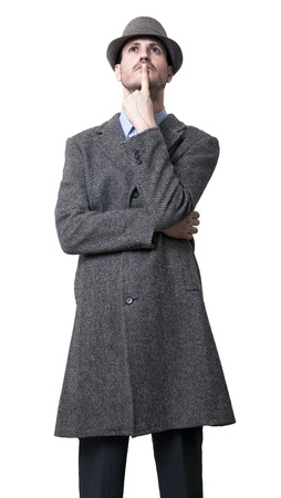 A young adult man dressed in a gray overcoat and a gray hat 1930's style, looking upwards with his finger on his lips, seems to be deep in thought. Isolated on white background.の写真素材