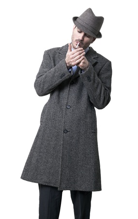 A person dressed in a gray overcoat and a gray hat. He's in the process of lighting a cigarette.
Isolated on white background.の写真素材