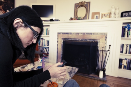An adult caucasian woman in her early 30's using her smartphone while sitting at a living room. Vintage coloring applied.の写真素材