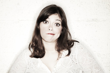 Portrait of a beautiful young woman staring into the camera. With her eyes wide open and upper lip in her mouth she's looking something in between shocked and apologetic, giving up on a situation.の写真素材