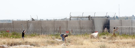 Bil'in, Palestine - May 17th, 2013: Three Palestinian youths throwing rocks towards the Israeli army force standing behind the wall of seperation that is between them. This is part of the weekly demonstration taking place in the village of Bil'in.のeditorial素材