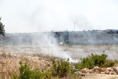 Bil'in, Israel - May 17th, 2013: A cloud of tear gas flying in the wind by the wall of separation between Palestine and Israel, with Israeli soldiers behind the wall.のeditorial素材