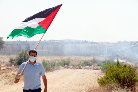 Bil'in, Palestine - May 17th, 2013: A palestinian protester holding the Palestine flag walking away from the wall of separation at a protest against the Israeli occupation.のeditorial素材