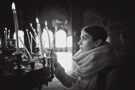 Young female lighting candles in a church during praying.Yellow votive candles burning.Woman praying to god at St. Alexander Nevsky Cathedral.Christianity.Strong christian religion faitの写真素材