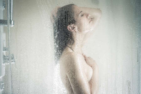 Relief and relaxation after long stressful day. Taking moment for yourself concept. Skincare, spa and aromatherapy. Unfocused portrait of a woman showering through the bath screen with little dropsの写真素材