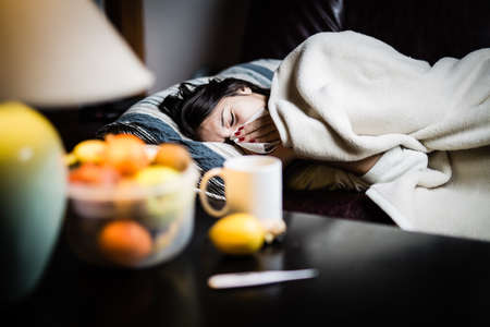 Sick woman in bed,calling in sick,day off from work.Thermometer to check temperature for fever.Vitamins and hot tea in front.Flu.Woman Caught Cold.Virus.Sick woman laying in bed under wool blanket Sick woman in bed,calling in sick,day off from work.Thermometer to check temperature for fever.Vitamins and hot tea in front.Flu.Woman Caught Cold.Virus.Sick woman laying in bed under wool blanket