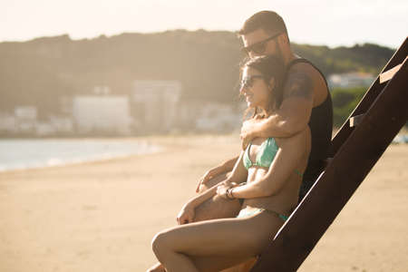 Romantic couple in hug watching sunrise sunset together.Young man and woman in love hugging and enjoying day at the beach.Flirting on summer vacation.Watching horizon,waves.Romance.Young love.Dateの写真素材