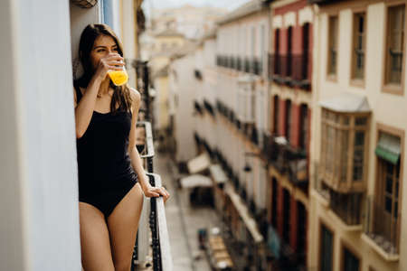 Young european woman spending free time home.Self care,staying home.Enjoying view on the balcony.Relaxing at home.Hotel room balcony view,vacation in Europe.Drinking orange juice in the morningの写真素材