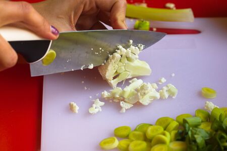 A young woman chops cauliflower with a big knife.の写真素材