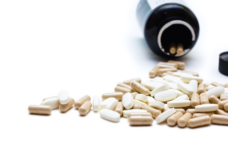 White and brown capsules spilling from a bottle of a prescription; shallow depth-of-field image. Isolated over white background.の写真素材