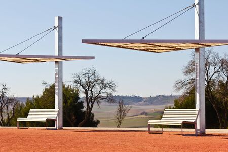 Benches with modern canopies in a park, on red sand with a nice view of nature behind, selective focus.の写真素材