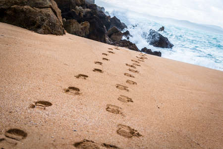 Beach with footprints towards the sea with waves crushing at the background.の写真素材