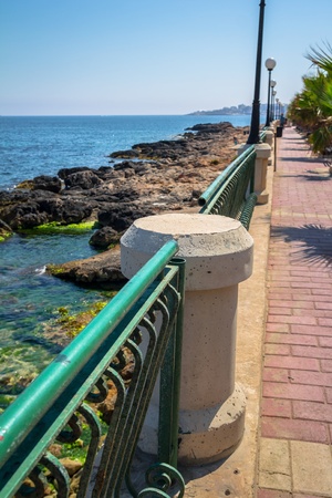 Promenade on the coast of Malta with a handrail separating palm trees and the beach の写真素材
