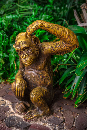Golden chimpanzee statue surrounded by nature scratching its head 