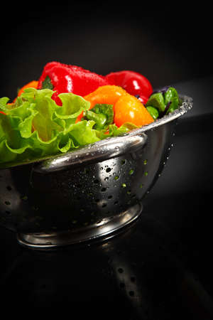 Freshly washed fresh vegetables in a metal colander isolated over black background  の写真素材