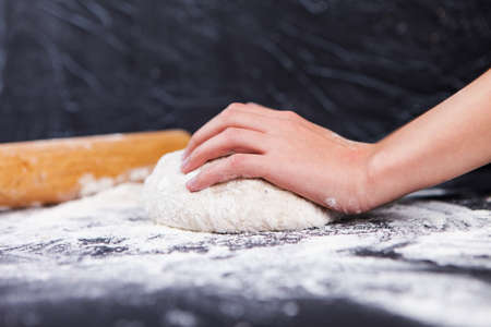 Baking preparing background. Female hands knead dough on the worktop.