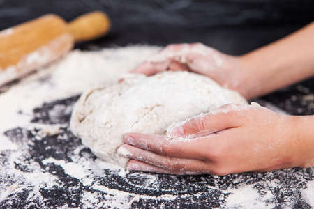 Baking preparing background. Female hands knead dough on the worktop.